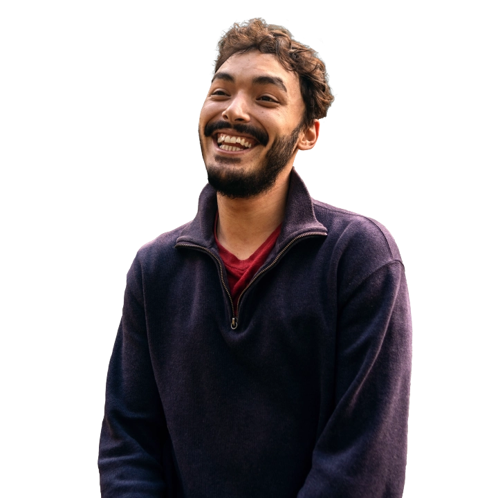 A young man with short hair and a beard wearing a purple sweater smiling big